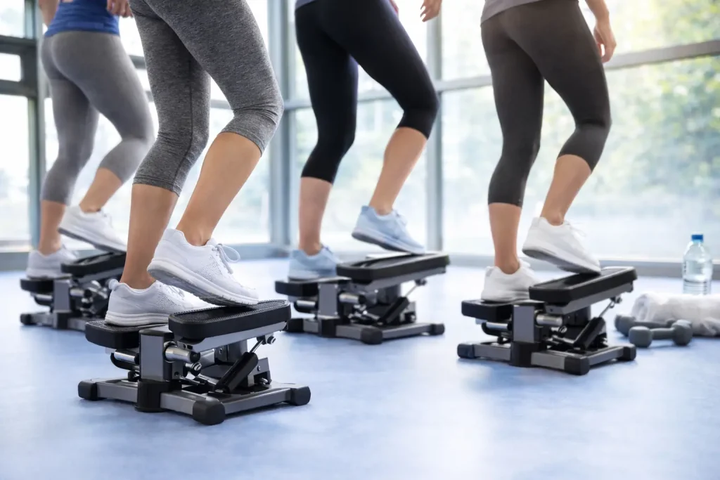 Plusieurs personnes utilisent un mini-stepper en salle de sport, jambes et pédales au premier plan